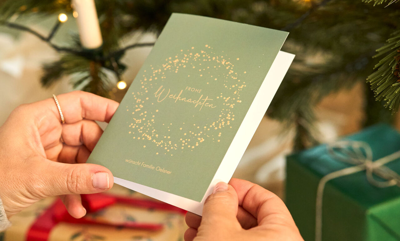 Eine Hand hält eine festliche Grußkarte mit dem Text „Frohe Weihnachten“.